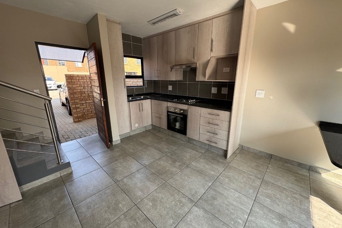 Modern kitchen featuring light wood cabinetry, granite countertops, built-in oven and hob, and tiled flooring, with direct access to the exterior.