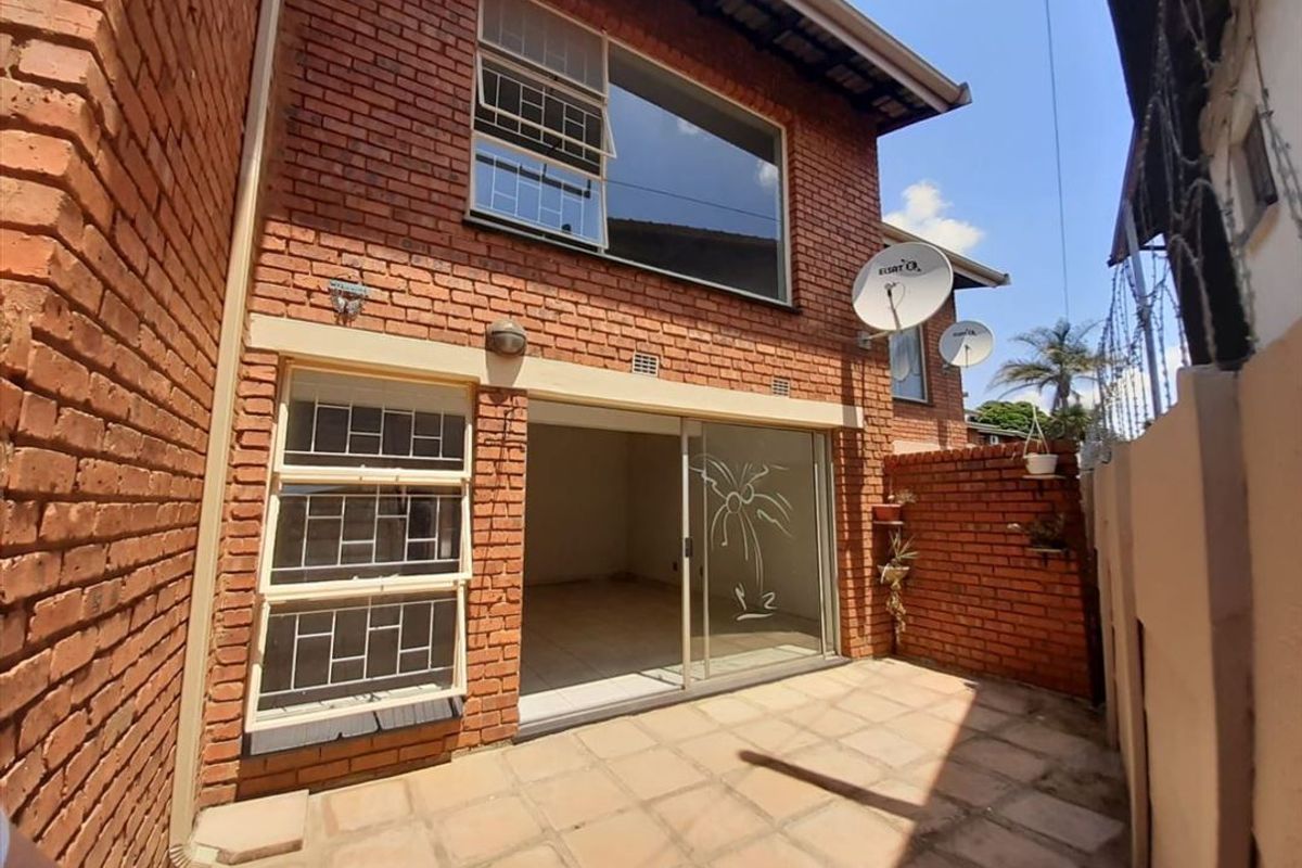 Rear exterior view of the townhouse featuring a paved patio area, exposed brick facade, and sliding glass door access to the interior living space.