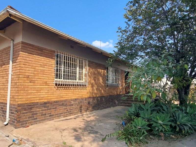 Rear exterior view of a face brick house featuring security bars on windows, exposed rafters, and a concrete pathway leading along the side.