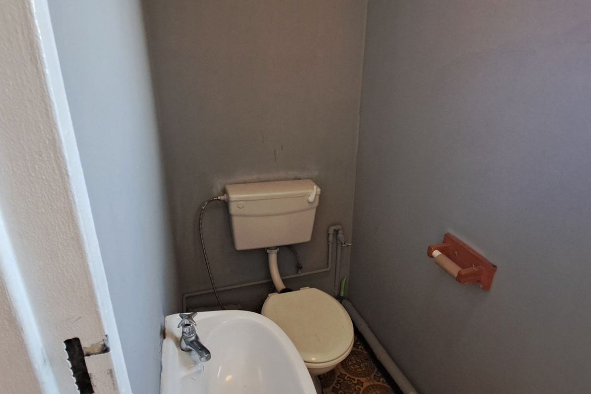 A small, functional bathroom featuring a standard toilet and a compact wall-mounted washbasin with exposed plumbing.