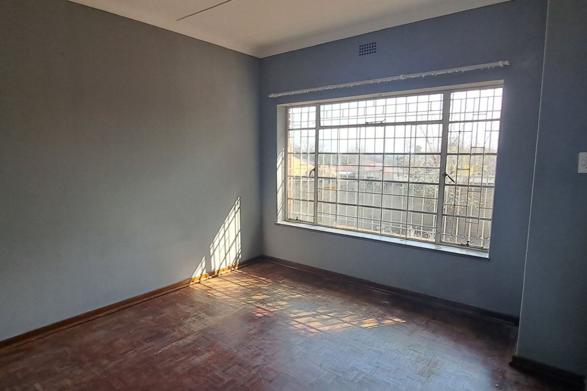 An empty bedroom featuring original parquet flooring, coved ceilings, and large windows fitted with security bars.