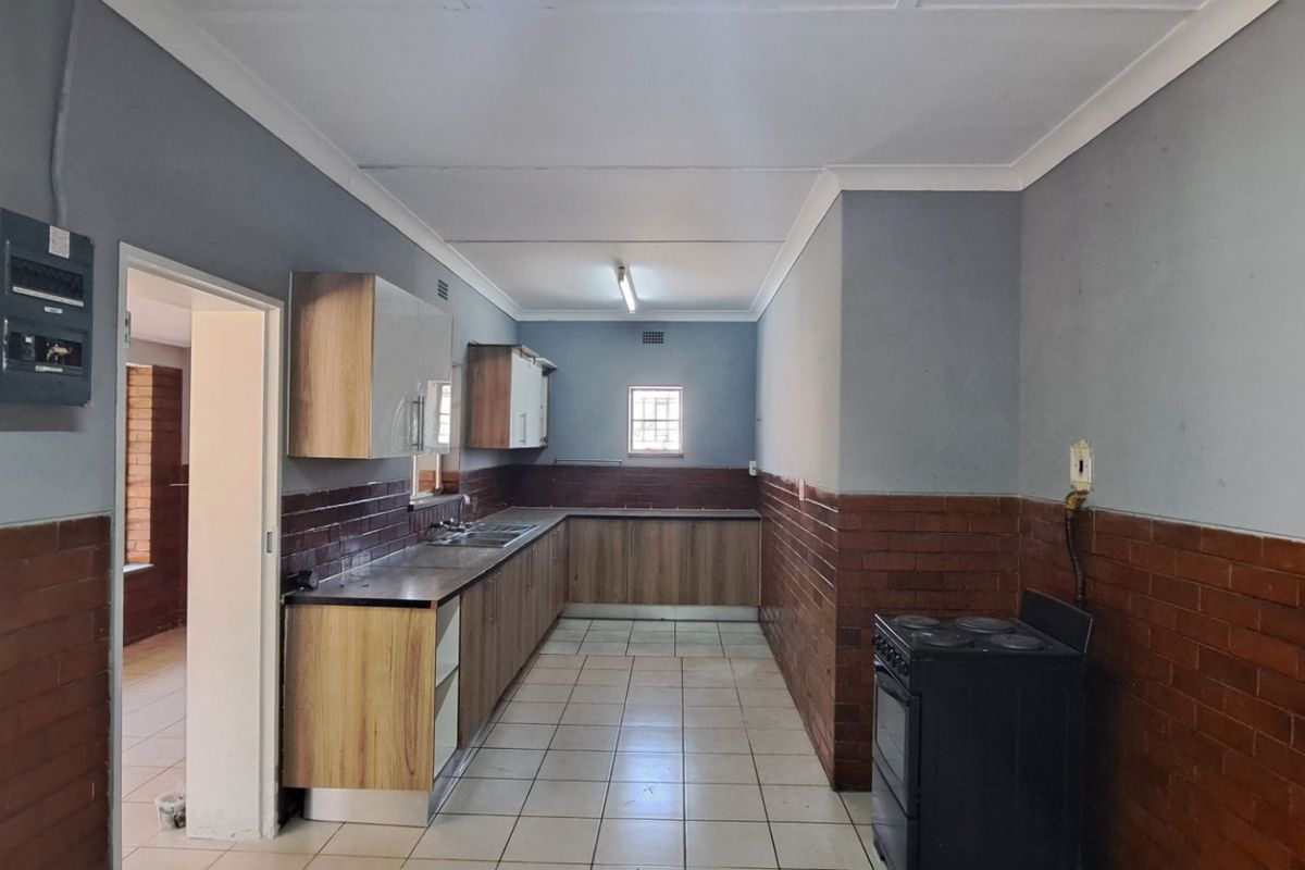 A functional kitchen featuring built-in cabinetry, stainless steel sink, tiled flooring, and brick wall accents, providing a clean and practical workspace.