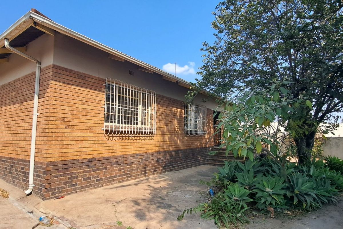 Rear exterior view of a face brick house featuring security bars on windows, exposed rafters, and a concrete pathway leading along the side.