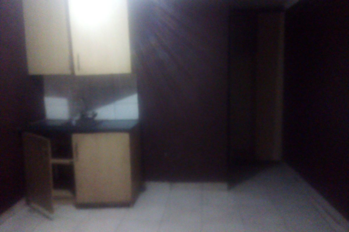 A small, dimly lit kitchen area featuring basic built-in cabinetry, a sink, and tiled flooring, currently in need of maintenance and improved lighting.