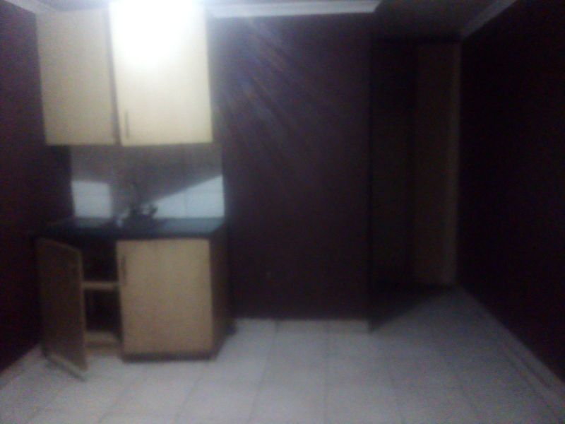 A small, dimly lit kitchen area featuring basic built-in cabinetry, a sink, and tiled flooring, currently in need of maintenance and improved lighting.