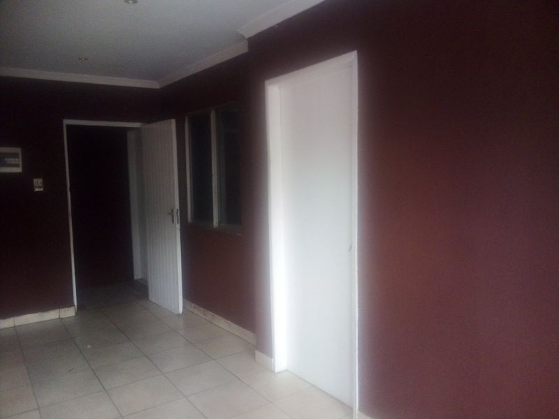 An empty hallway featuring tiled flooring, recessed downlighting, and dark-painted walls with multiple internal door access points.