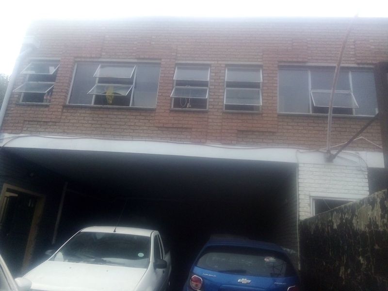 Front elevation of a commercial building featuring a brick facade with multiple top-hung windows and a covered ground-level parking area.