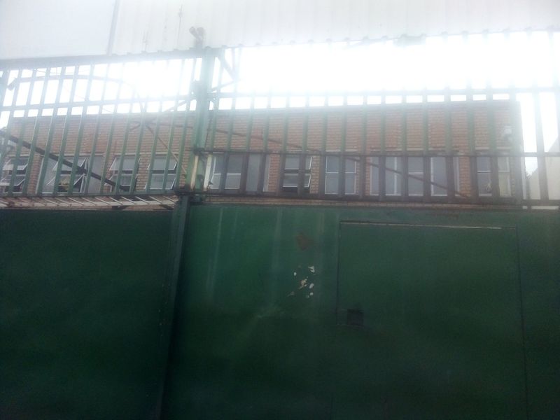 A commercial property exterior featuring a large green metal security gate and a brick facade with multiple steel-framed windows.
