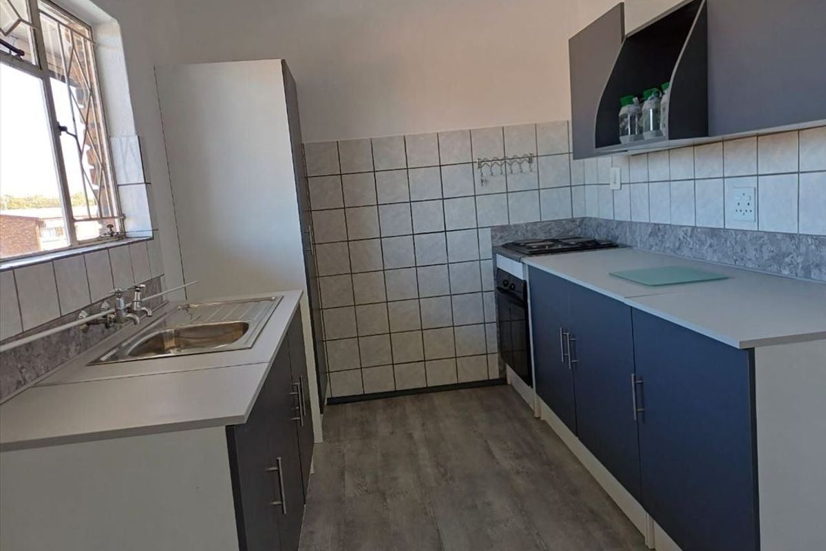 A clean, functional kitchen featuring modern dark cabinetry, laminate countertops, a built-in oven and hob, and a tiled backsplash.