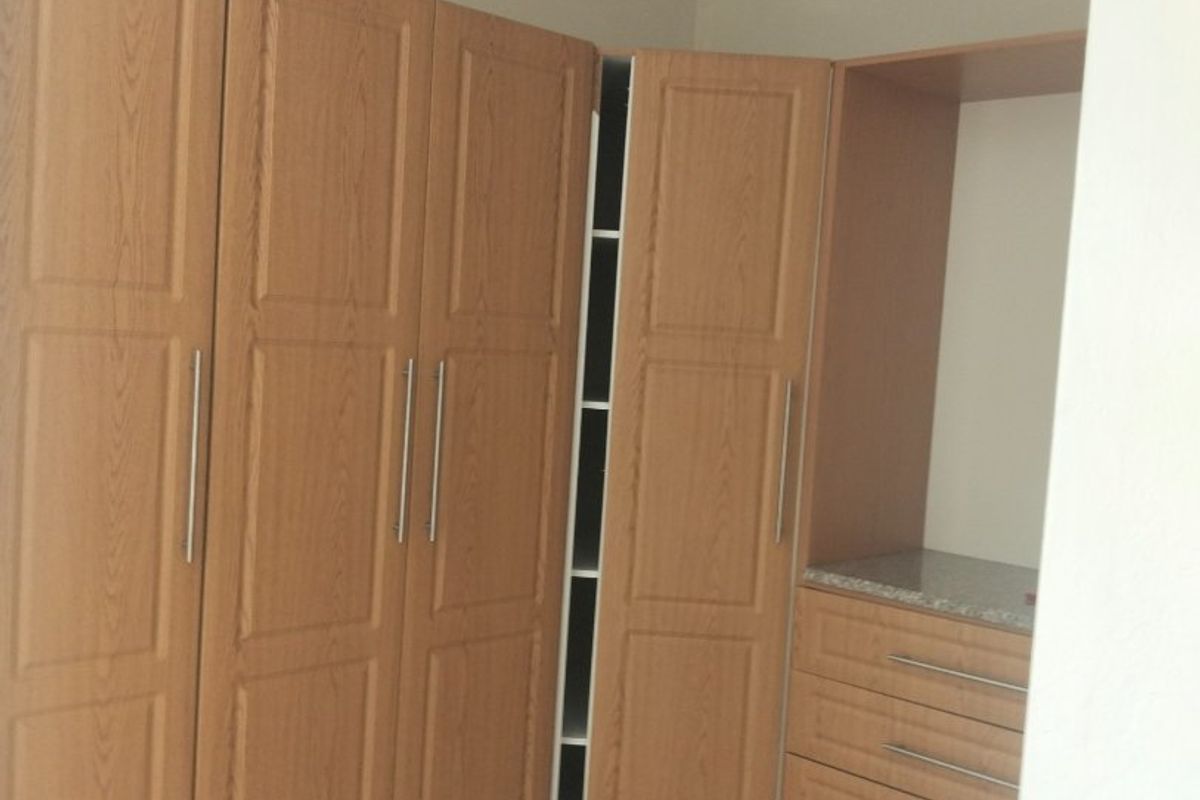 A bedroom featuring built-in wooden cupboards with integrated drawers and tiled flooring.