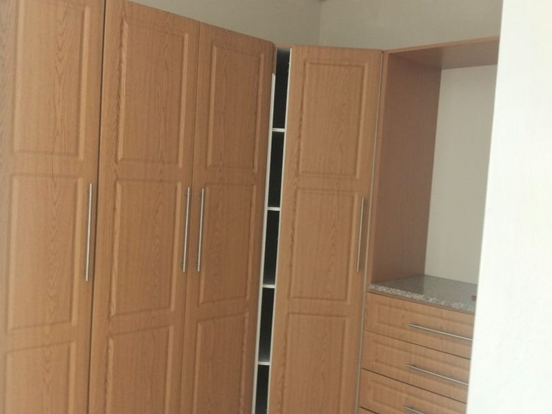A bedroom featuring built-in wooden cupboards with integrated drawers and tiled flooring.