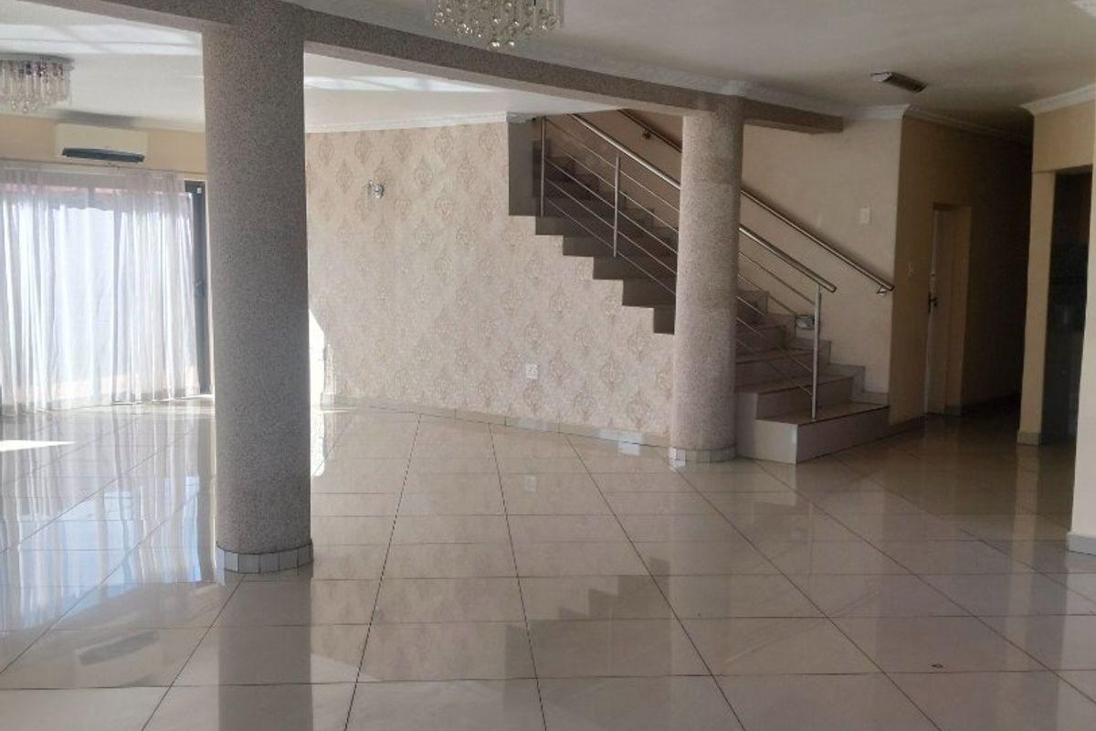 Spacious open-plan living area featuring polished tile flooring, structural columns, and a staircase with a modern stainless steel balustrade.