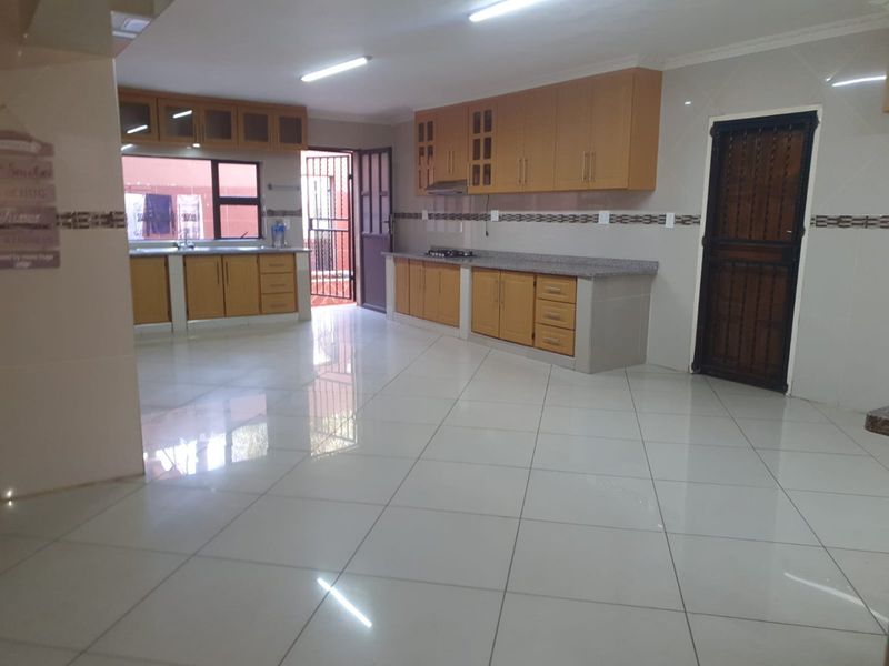 Spacious kitchen featuring light wood cabinetry, granite countertops, a gas hob, and tiled flooring, offering a functional layout with direct outdoor access.
