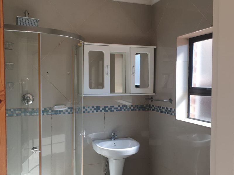 A functional bathroom featuring a curved glass shower enclosure, pedestal basin, and wall-mounted storage cabinet with tiled finishes.