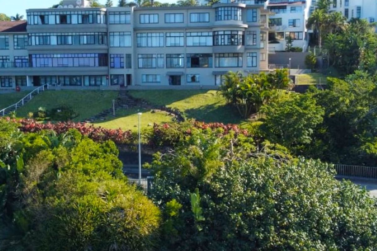 An elevated view of the apartment complex exterior, featuring a multi-story facade, landscaped grounds, and a swimming pool area.