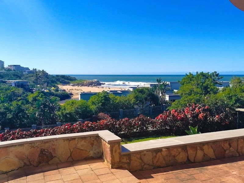 Spacious outdoor balcony featuring terracotta tiling and stone-clad walls, offering expansive views of the coastline and surrounding landscape.