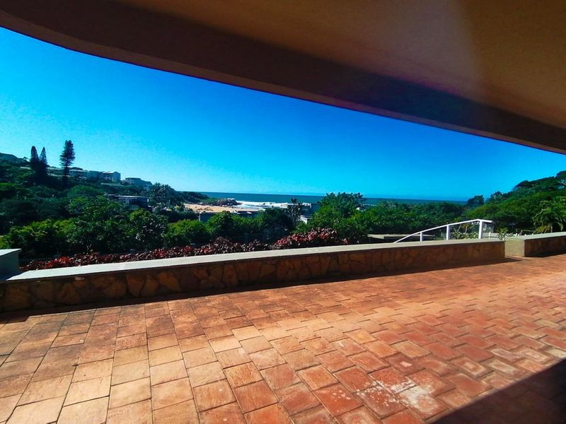 Spacious outdoor balcony featuring terracotta tiling and a stone-clad perimeter wall, offering expansive elevated views of the surrounding landscape and coastline.