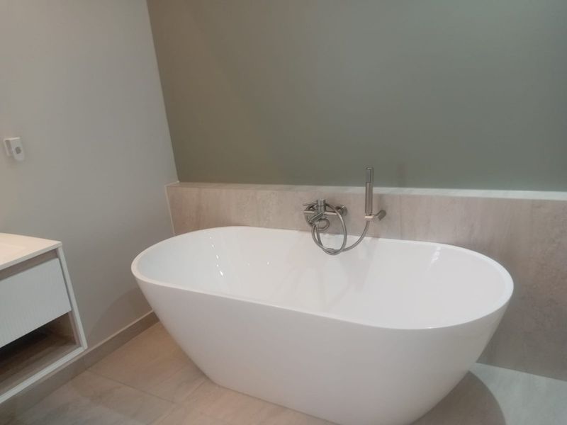 Modern bathroom featuring a sleek freestanding bathtub with wall-mounted mixer and handheld shower, complemented by a contemporary vanity unit.