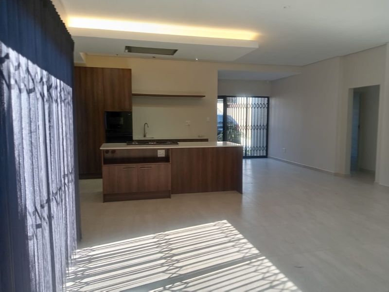Spacious open-plan living area featuring a modern kitchen with a central island, built-in appliances, and neutral tiled flooring throughout.
