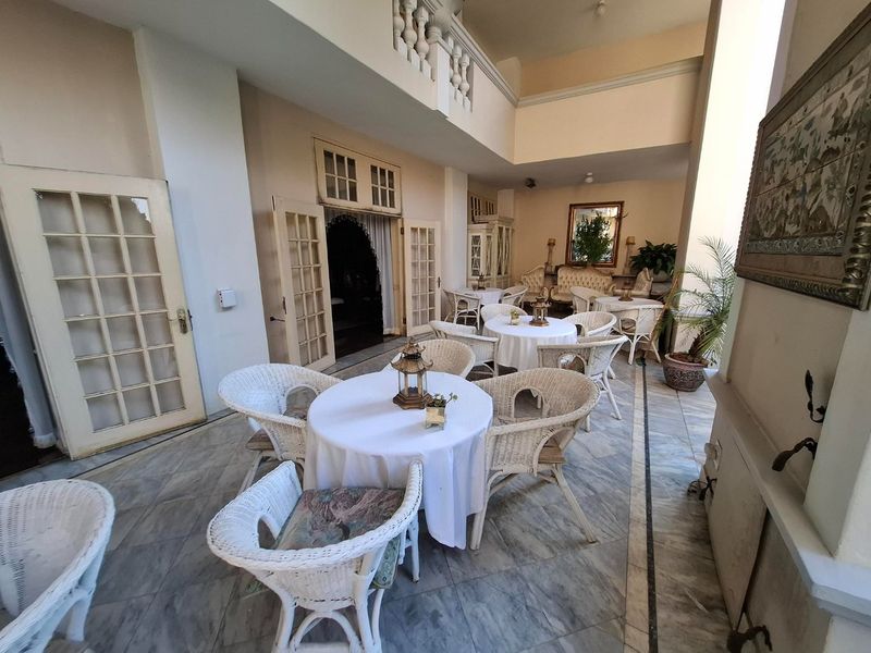 A spacious covered patio featuring elegant marble flooring, classic french doors, and a double-height ceiling with a decorative balustrade overlooking the area.