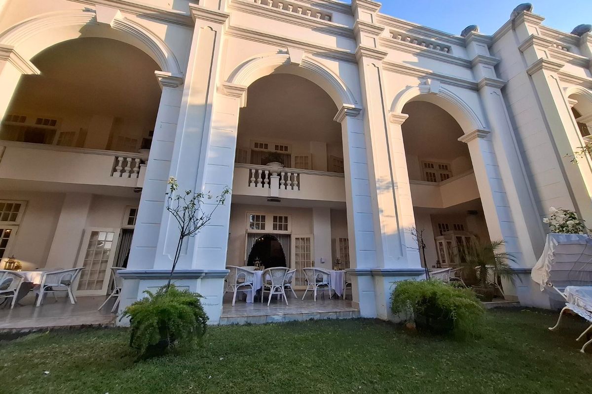 A grand double-story rear facade featuring elegant arched colonnades, a spacious tiled patio, and classic architectural detailing overlooking a manicured garden.