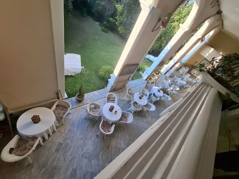 A spacious covered patio featuring tiled flooring and classic arched columns, overlooking a lush green garden area.