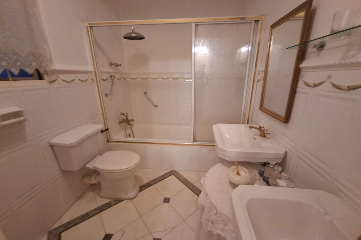 A functional bathroom featuring a bathtub with a shower screen, pedestal sink, and classic tiled finishes throughout.