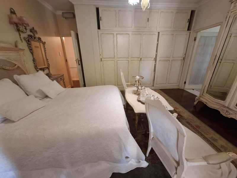 A spacious bedroom featuring extensive built-in cabinetry, crown molding, and dark hardwood flooring, offering a classic aesthetic with ample storage space.
