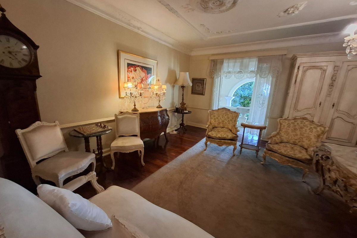 A formal living room featuring hardwood flooring, ornate ceiling roses, decorative molding, and an arched window with access to an outdoor area.