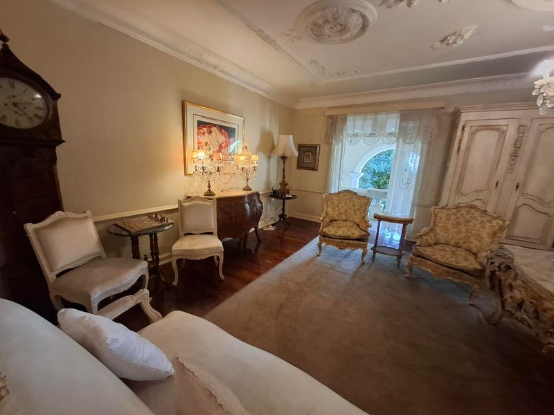 A formal living room featuring hardwood flooring, ornate ceiling roses, decorative molding, and an arched window with access to an outdoor area.
