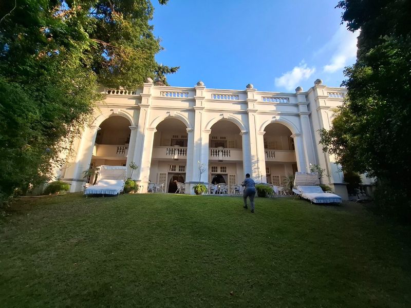 A grand rear elevation featuring a double-story arched colonnade, classic balustrade detailing, and expansive covered patio areas overlooking a manicured lawn.