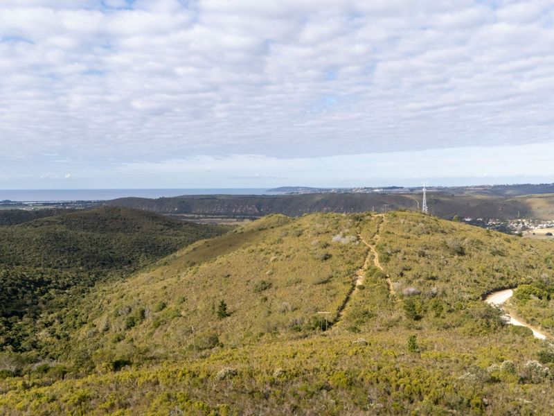 An aerial view of the vacant residential land, showcasing the natural hilly landscape, surrounding vegetation, and distant coastal horizon.