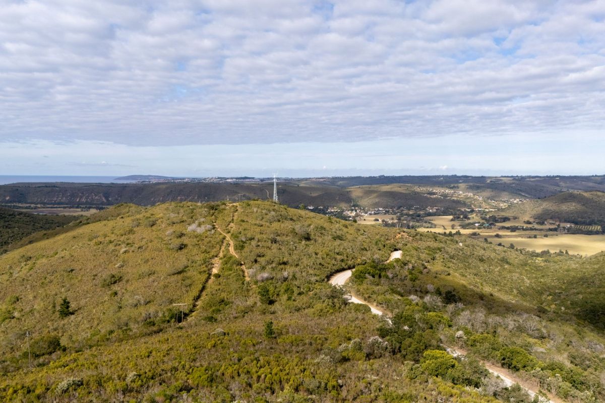 An aerial view of the vacant residential land featuring natural hilly terrain, native vegetation, an unpaved access road, and distant landscape views.