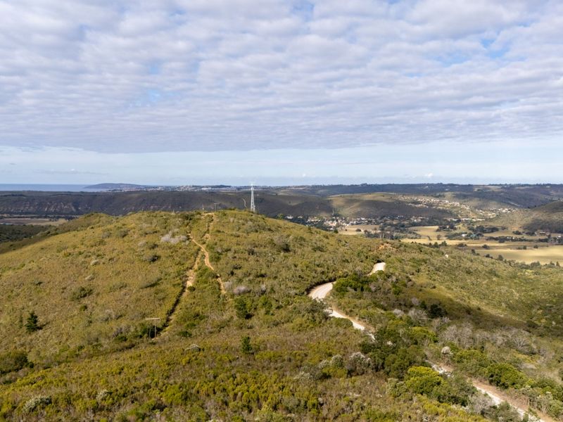 An aerial view of the vacant residential land featuring natural hilly terrain, native vegetation, an unpaved access road, and distant landscape views.