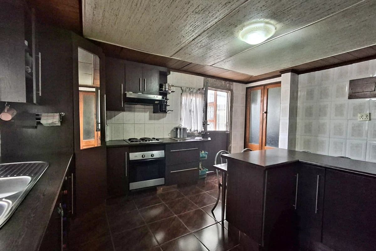 A functional kitchen featuring dark cabinetry, built-in oven and hob, double sink, and tiled flooring, offering a solid foundation for modern updates.