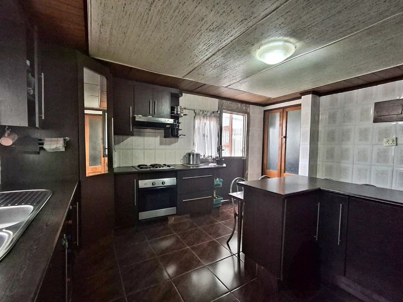 A functional kitchen featuring dark cabinetry, built-in oven and hob, double sink, and tiled flooring, offering a solid foundation for modern updates.