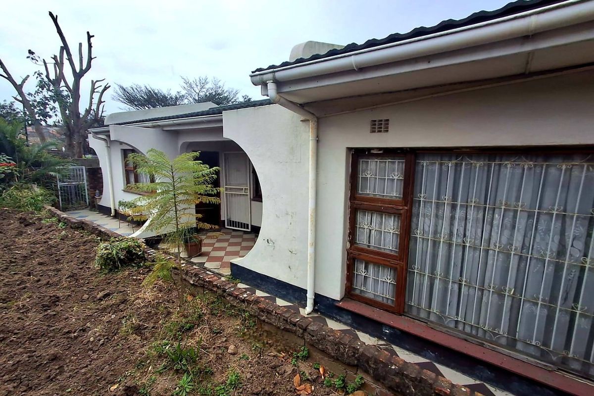 Rear exterior view of the house featuring arched architectural details, a tiled patio area, and security bars on the windows.