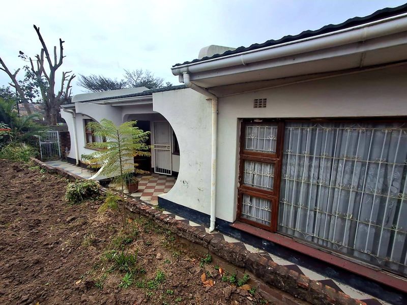 Rear exterior view of the house featuring arched architectural details, a tiled patio area, and security bars on the windows.