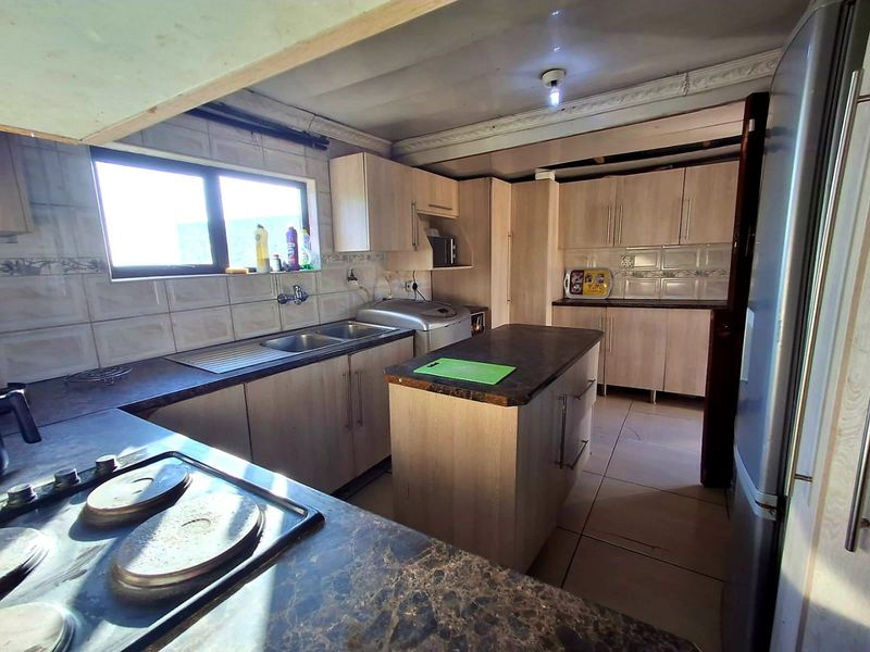 A functional kitchen featuring light wood-finish cabinetry, a central island, dark laminate countertops, and tiled flooring, requiring some cosmetic updates to the ceiling and finishes.