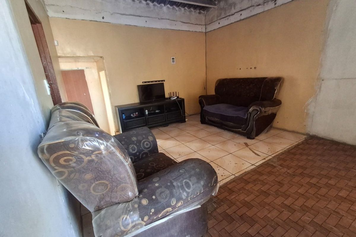 A living room area featuring ceramic floor tiles and an exposed roof structure, requiring significant cosmetic updates and finishing to improve the interior aesthetic.