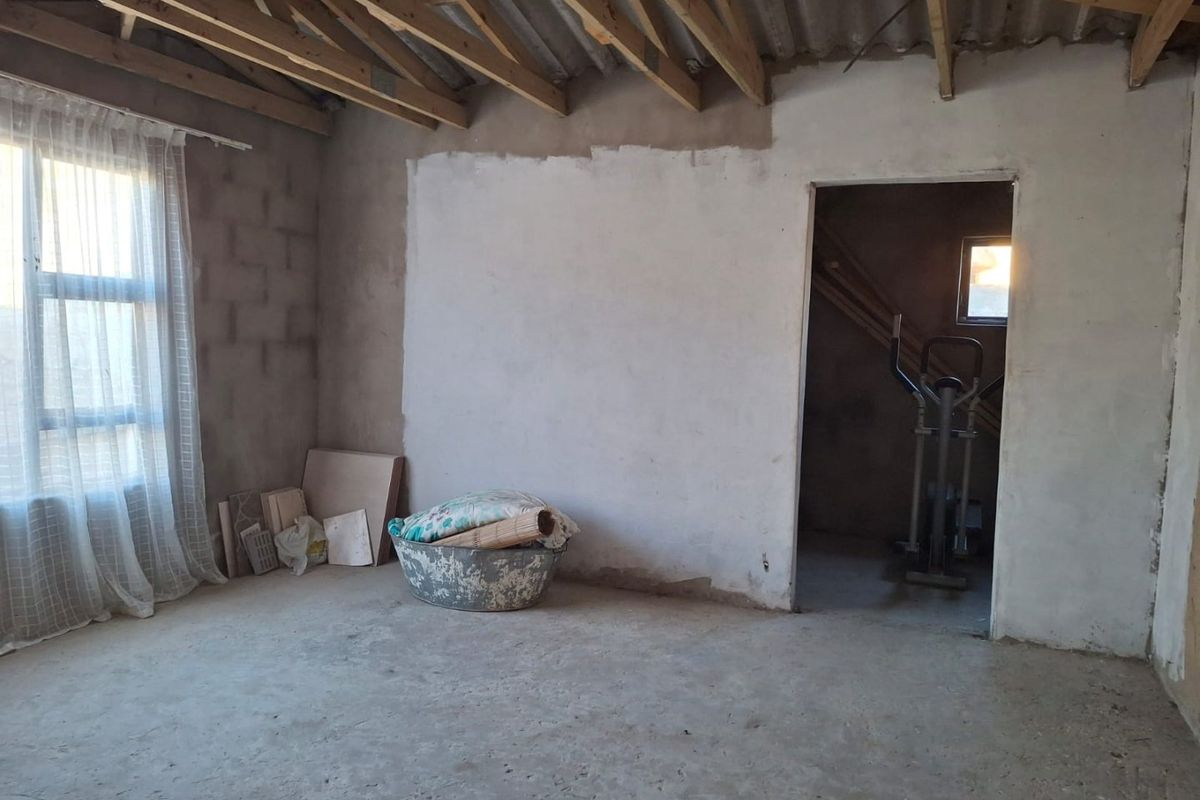 An unfinished bedroom space featuring exposed timber roof trusses, raw blockwork walls, and cement screed flooring, offering a blank canvas for renovation.