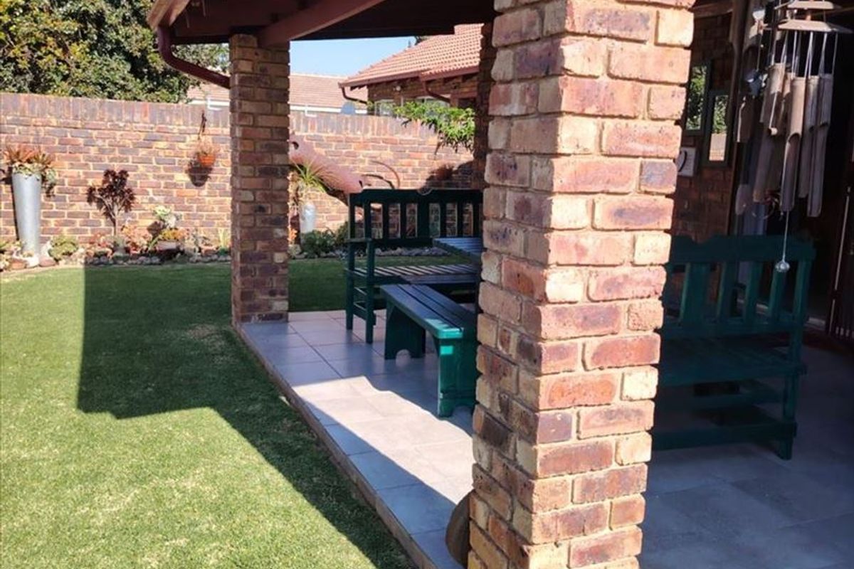 A covered patio area featuring brick pillars and tiled flooring, overlooking a private garden space.