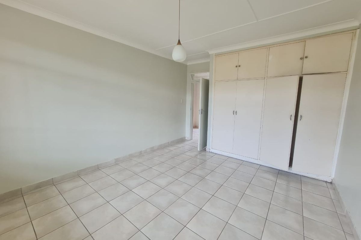 An empty bedroom featuring tiled flooring, coved ceilings, and built-in storage cupboards.