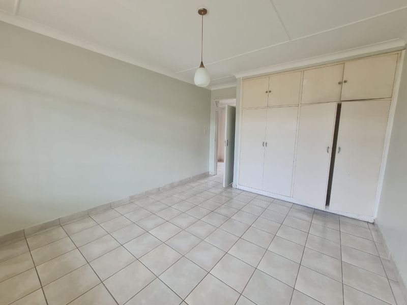An empty bedroom featuring tiled flooring, coved ceilings, and built-in storage cupboards.