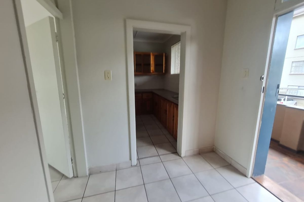 An empty kitchen area featuring wooden cabinetry and tiled flooring, with direct access to an adjacent balcony space.