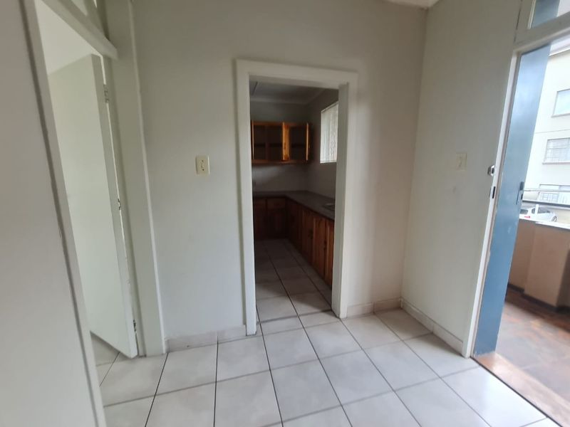 An empty kitchen area featuring wooden cabinetry and tiled flooring, with direct access to an adjacent balcony space.