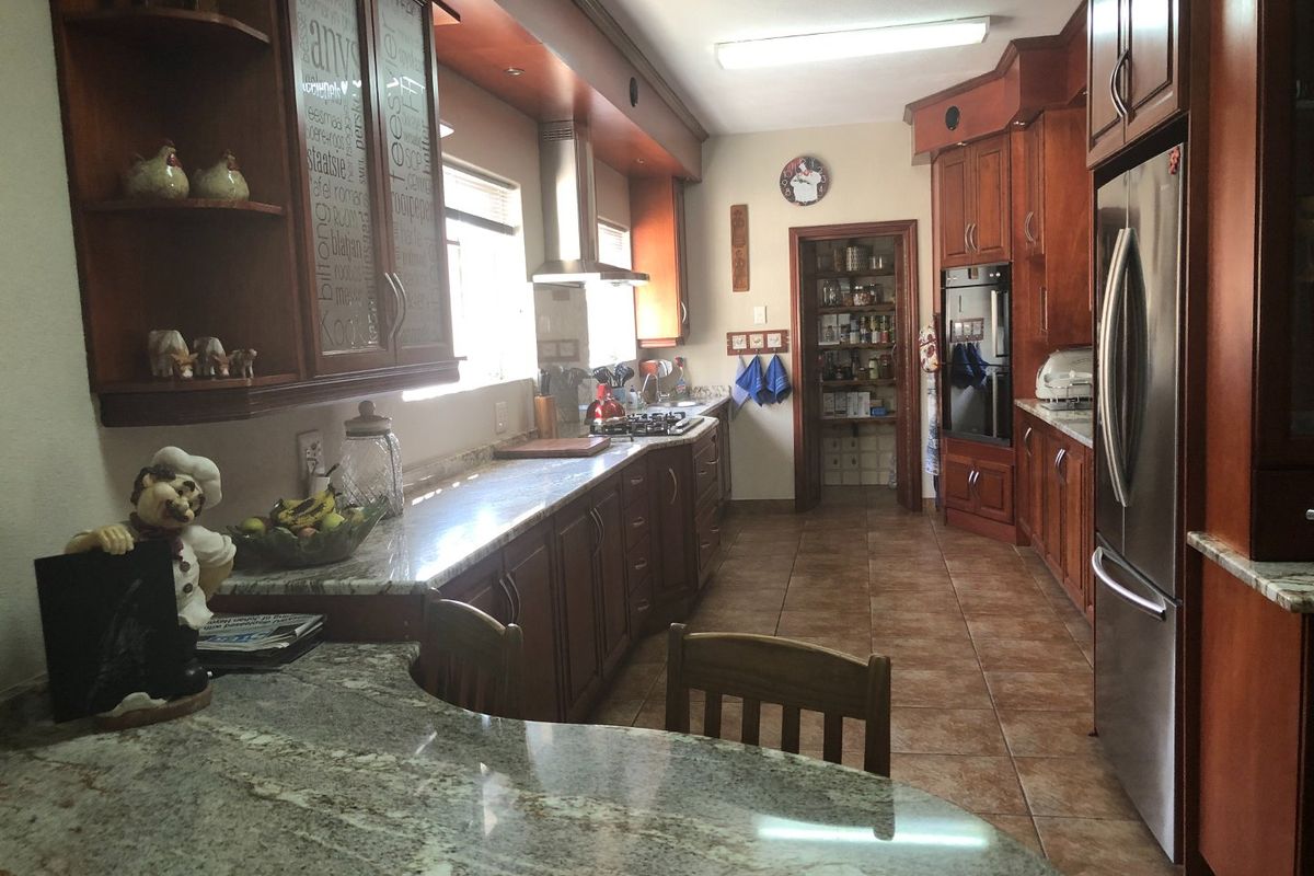 Spacious kitchen featuring extensive wooden cabinetry, granite countertops, built-in appliances, and a convenient walk-in pantry with tiled flooring throughout.