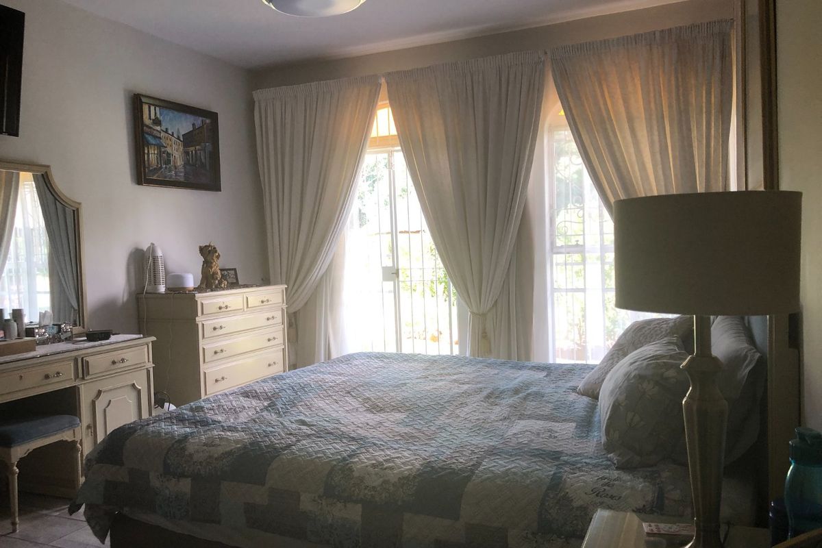 A comfortable bedroom featuring tiled flooring, a ceiling light fixture, and access to the exterior through a secure gate.