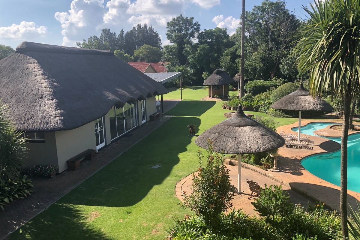 Spacious rear garden featuring a swimming pool, paved deck with thatched umbrellas, and a large house with a traditional thatched roof.
