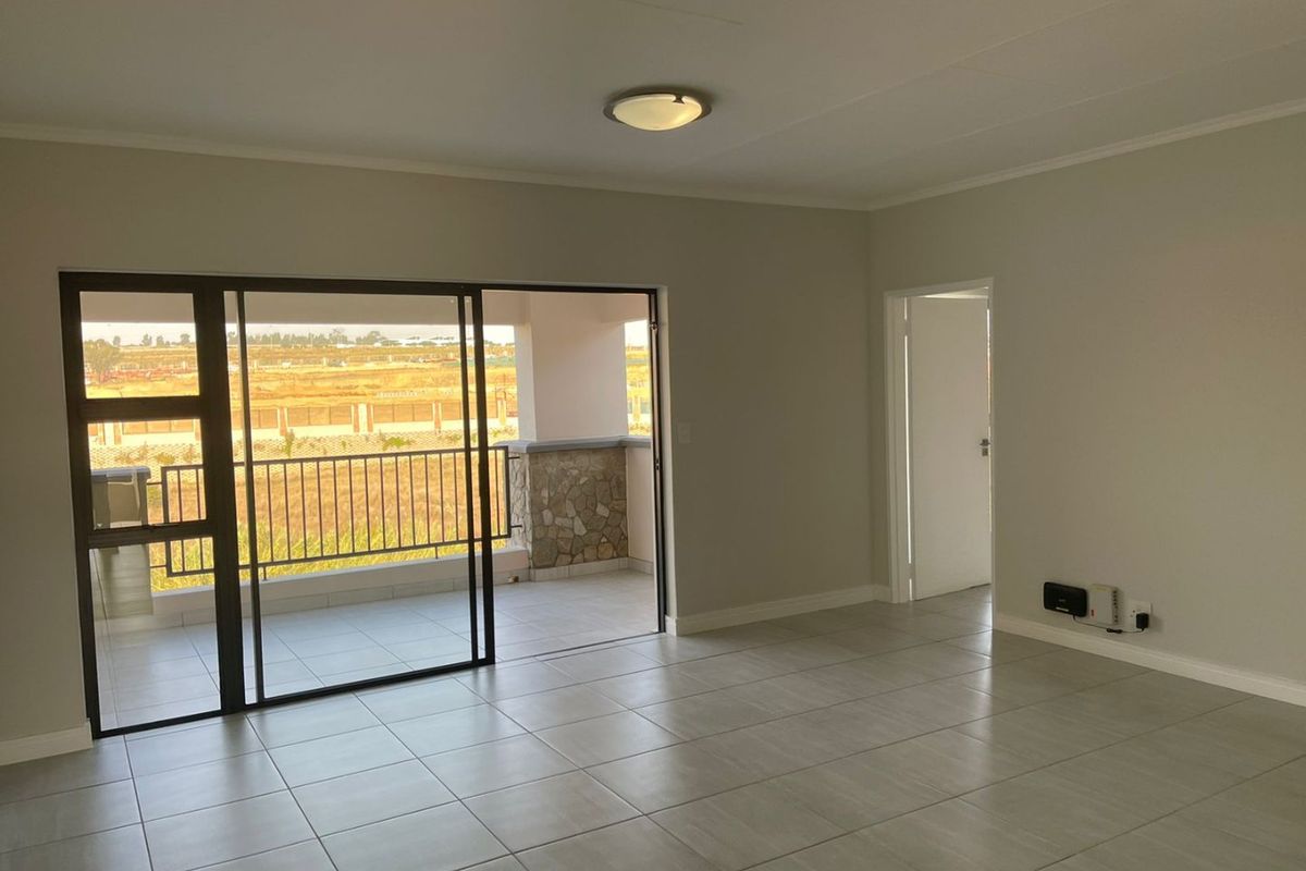 A bright, open-plan living area featuring neutral tiled flooring and a large sliding glass door providing direct access to a private balcony.